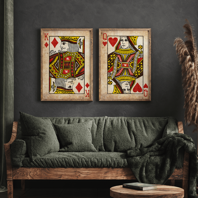 A set of two framed playing card wall art pieces, depicting the King and Queen cards, hung on a wall above a grey sofa with a fur throw.