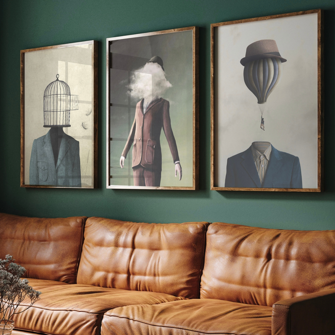 A set of three framed art prints hanging on a wall above a brown leather sofa, featuring abstract and surreal imagery.